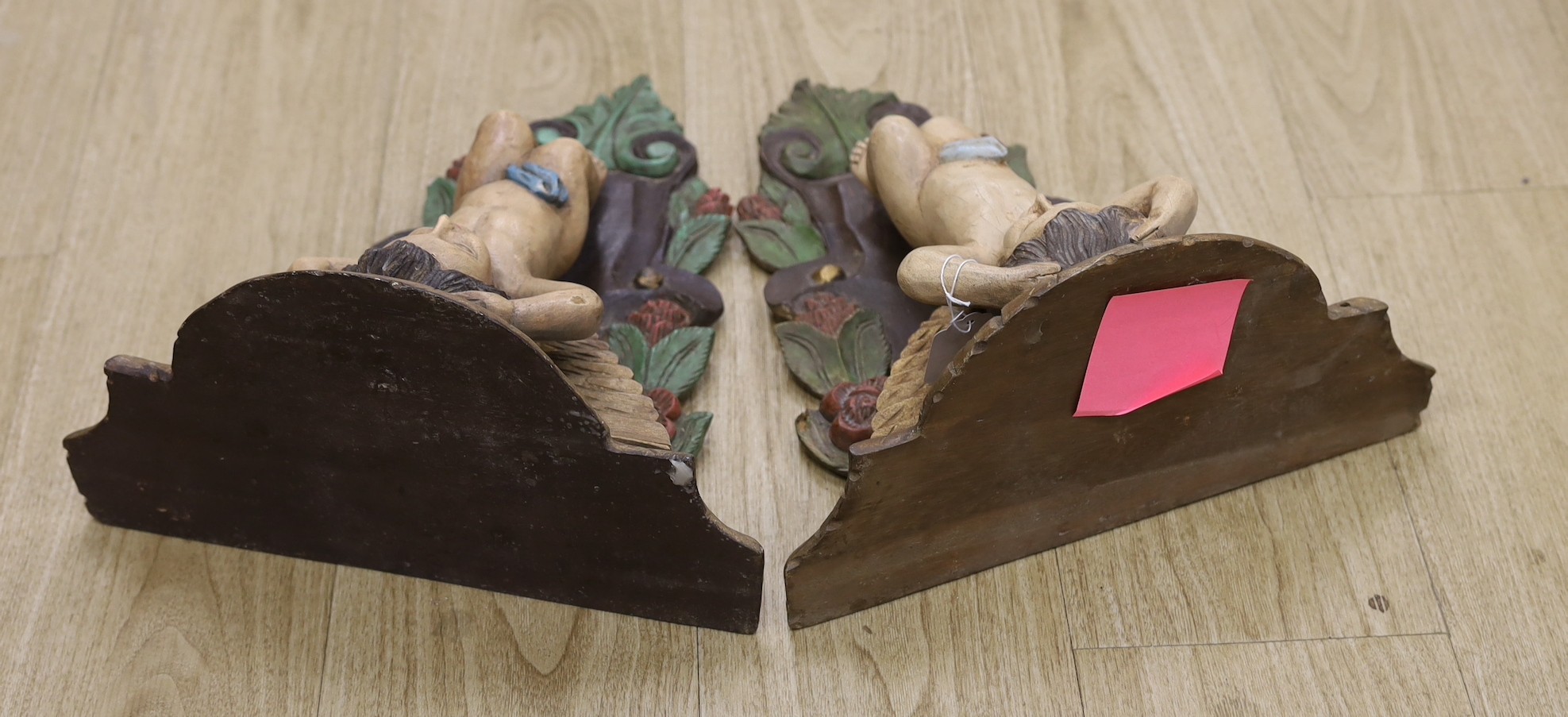 A pair of painted wooden cherubic wall brackets, 42cm tall